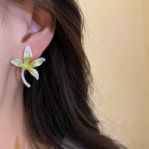 Detailed view of an elegant white and green floral stud earring worn on a person's ear