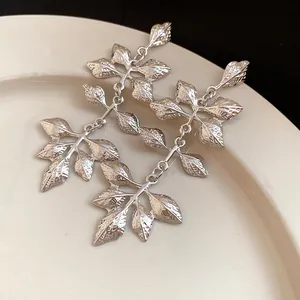 Gros plan de boucles d'oreilles en argent à pampilles en feuilles sur une assiette.