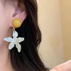 Close-up of yellow resin stud and white star flower drop earrings for summer beach style
