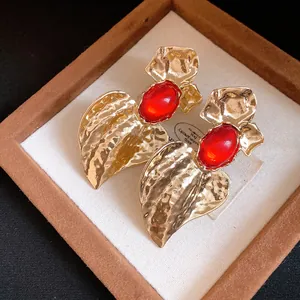 Macro view of statement heart-shaped textured gold earrings with red resin stones in box.