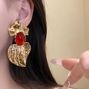 Detailed macro view of an oversized gold hammered earring with a red resin cabochon