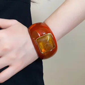 Detail view of stylish amber acrylic bangle with a square textured stone in a gold frame