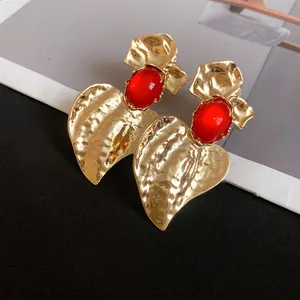 Close-up detail of gold heart-shaped earrings with red resin stones and hammered texture
