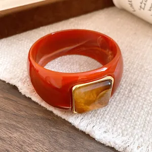 Close-up of reddish-brown acrylic bangle with square amber resin inlay and gold trim.