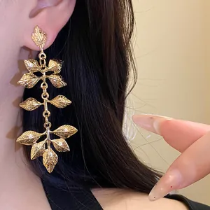 Gros plan détaillé de boucles d'oreilles à pampilles en feuilles d'or portées par un modèle