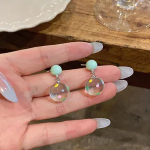 Close-up detail of clear resin earrings with colorful polka dots and mint green beads