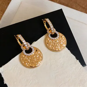 Detail shot of 18k gold-plated earrings with zircon and textured circular pendants.
