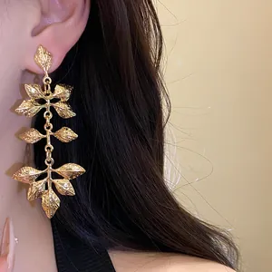 Détail de boucles d'oreilles pendantes en métal doré avec motif de feuilles froissées