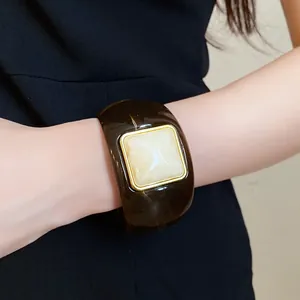 Close-up detail of a wide amber acrylic bangle featuring a square cream stone element