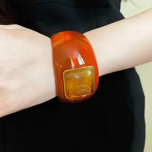 Close-up of a wide amber acrylic bangle with a square golden frame detail.