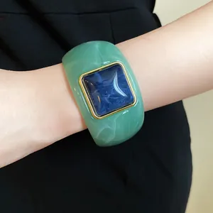 Close-up view of a green acrylic square bangle with a blue marbled center piece on a wrist