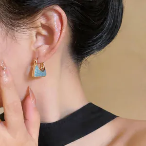 Detailansicht von 18 Karat vergoldeten Creolen mit blauen Steintaschen-Anhängern am Ohr