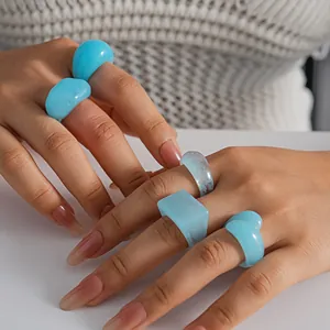 Detail showing a five-piece set of blue resin marbled geometric rings on hands.