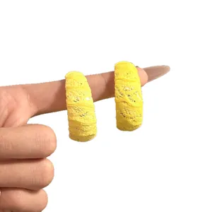 Pendientes de aro en forma de C de encaje amarillo brillante mostrados en un dedo.