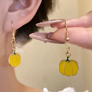 Close-up detail of yellow drip oil pumpkin dangle earrings being worn and held by a hand