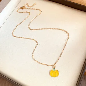 Detailed macro view of yellow enameled pumpkin pendant on a dainty gold necklace chain