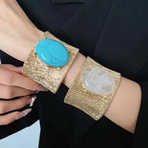Dettaglio di bracciali a polsino in metallo dorato con grandi pietre ovali retrò