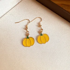 Detail view of yellow enameled pumpkin earrings with gold hooks for fall theme
