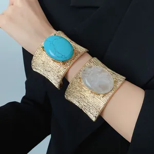 Dettaglio macro di un bracciale a polsino dorato con grandi pietre ovali turchese e quarzo