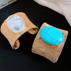 Dettaglio di bracciali rigidi dorati retrò con grandi pietre ovali turchesi e bianche