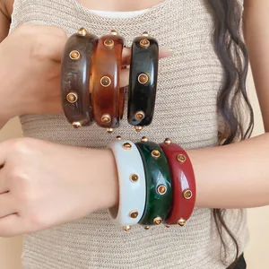 Nahaufnahme von Vintage-Harzarmbändern mit goldenen Nieten am Handgelenk eines Models