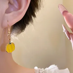 Detailed view of a sweet yellow enamel pumpkin pendant earring worn on a female ear
