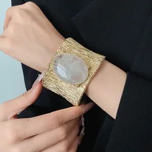 Vista dettagliata di un bracciale dorato vintage con una grande pietra bianca ovale.