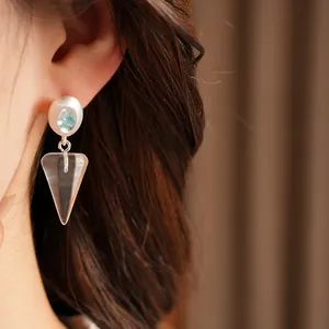 Close-up detail of ice blue zircon and clear resin cone drop earring worn on a model ear