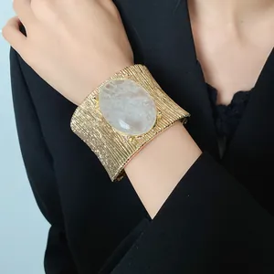 Dettaglio di un bracciale a fascia dorato vintage con pietra ovale indossato da una modella