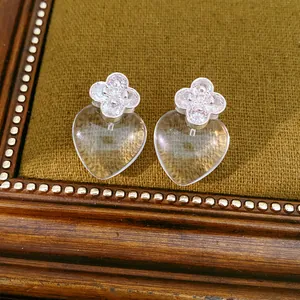 Close-up of elegant clear resin heart earrings with zircon four-leaf clover studs