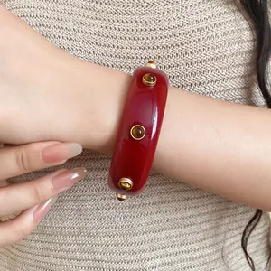 Detailansicht eines roten Vintage-Resin-Armreifs mit goldenen Nieten am Handgelenk