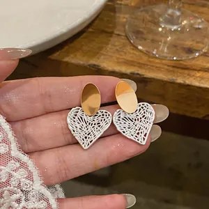 Detailed macro view of hollowed-out heart stud earrings in gold and silver metal tones.