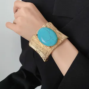 Bracciale rigido dorato vintage con grande pietra turchese ovale sul polso del modello