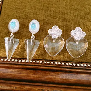 Close-up of elegant silver needle earrings featuring blue zircon and clear resin charms