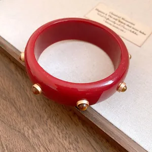 Detailansicht eines roten Vintage-Harzarmbands mit dekorativen goldfarbenen Nietendetails