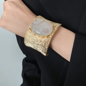 Dettaglio ravvicinato di un bracciale a polsino in metallo dorato con pietra ovale