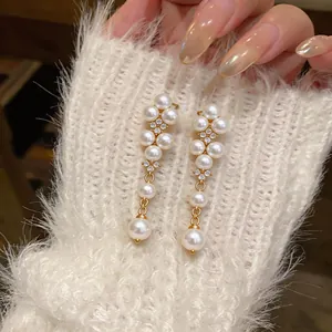 Close-up of elegant gold drop earrings with white pearls and zircon on soft white knitwear.