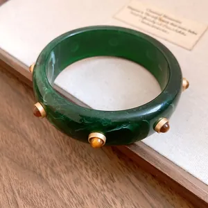 Detailansicht eines grünen Retro-Harzarmbands mit goldenen Nieten und Marmorierungseffekt.