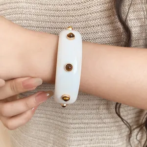 Detailansicht eines weißen Harzarmreifs mit braunen Nieten im Vintage-Stil an Handgelenk