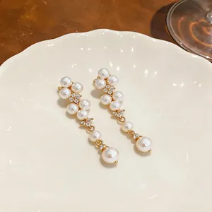 Close-up detail of elegant French style pearl and zircon dangle earrings on a white ceramic plate.