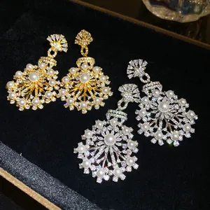 Détail de boucles d'oreilles fleuries dorées et argentées avec perles et pierres CZ