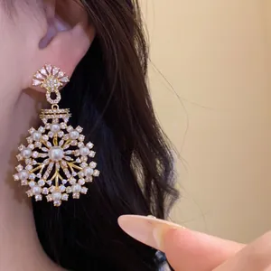 Détail en gros plan d'une boucle d'oreille fleur dorée ornée de perles et de zircons