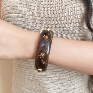 Detailansicht eines Vintage-Harzarmbands mit Marmorierung und goldenen Nieten am Handgelenk.