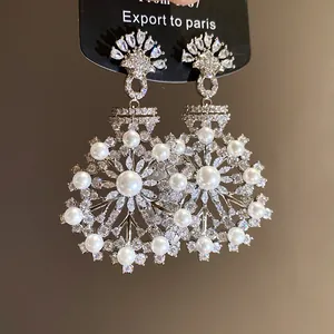 Vue détaillée des boucles d'oreilles fleuries avec perles blanches et zircons brillants
