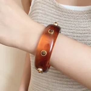 Nahaufnahme eines Vintage-Armreifs aus bernsteinfarbenem Harz mit goldenen Nieten-Akzenten