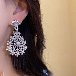 Élégantes boucles d'oreilles pendantes fleurs avec zircons et perles sur l'oreille