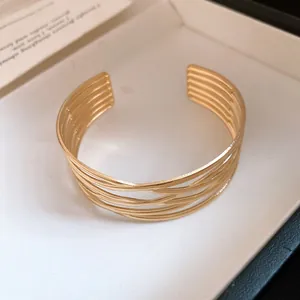 Nahaufnahme eines eleganten, goldfarbenen, mehrlagig gestreiften, offenen Armreifs für Damen