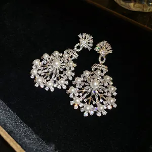 Vue détaillée de boucles d'oreilles pendantes fleurs en zircons et perles sur velours noir.