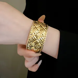 Nahaufnahme eines breiten goldenen Armreifs mit einer eleganten Faltenstruktur am Handgelenk