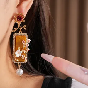 Gros plan de boucles d'oreilles fleurs vintage avec résine ambrée, strass et perles.